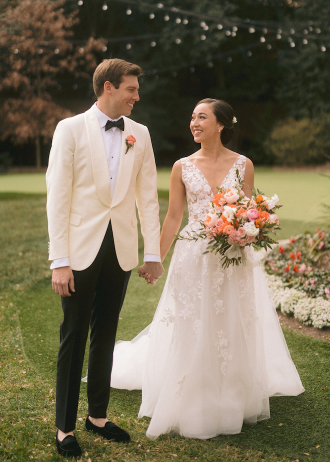 The bride and groom hold hands at their orange, pink and white wedding ceremony.