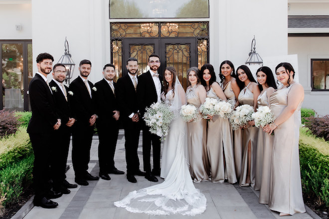 The bride and groom smiling with the wedding party in front of the white wedding venue.