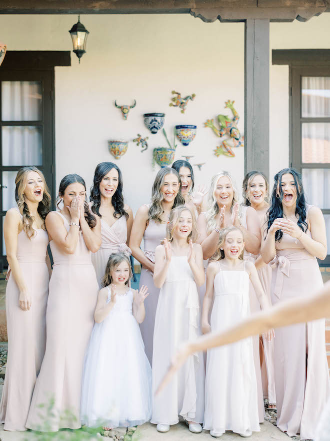 The bride's bridesmaids and flower girls react to seeing the bride outside in her wedding gown. 