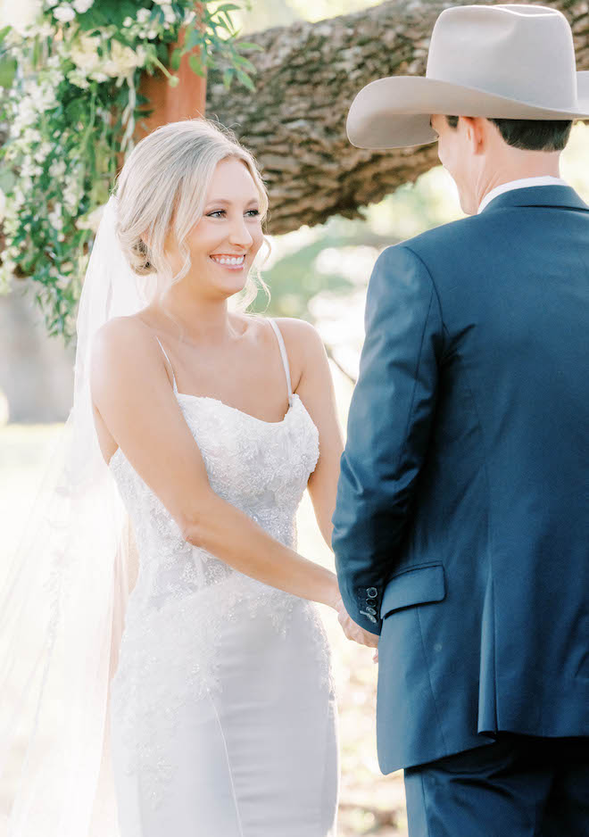 The bride smiles as she holds hands with the groom on the alter at their outdoor wedding ceremony.