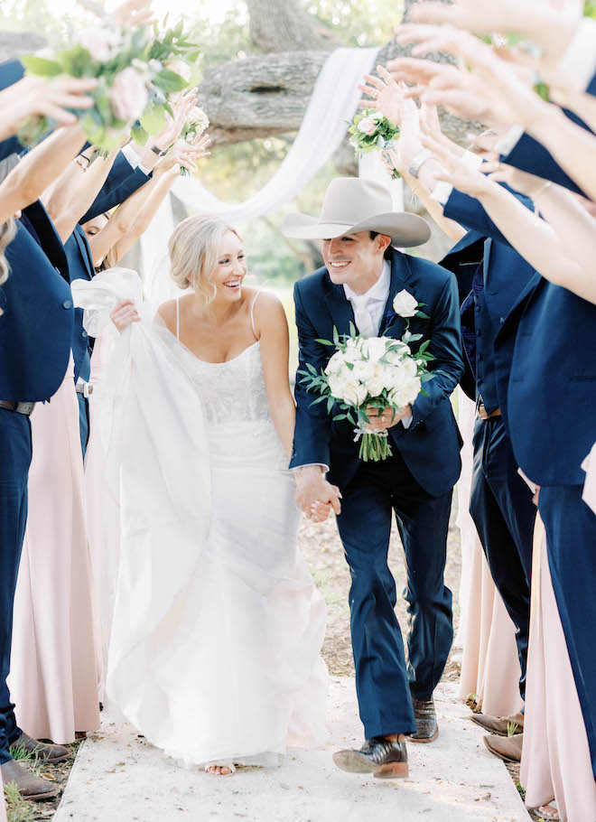 The bride and groom hold hands as they celebrate with their wedding party outside.