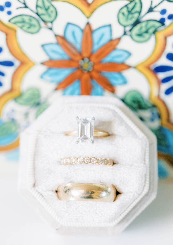 The bride and groom's wedding bands sit in a felt box in front of a colorful wall.