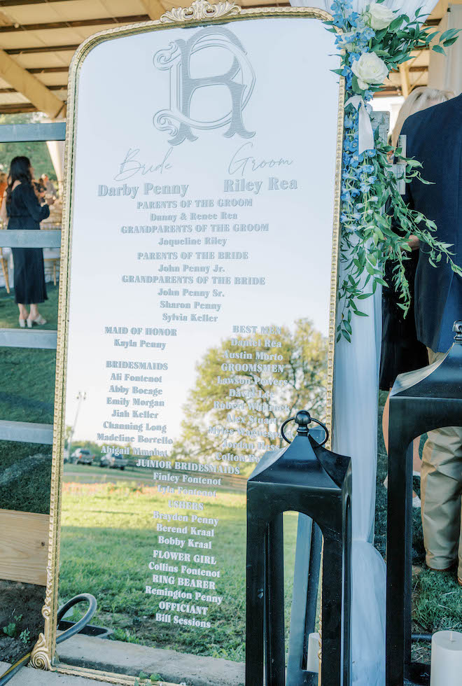 A mirror with writing is placed at the front of the reception venue with the bride and groom's family and wedding party's names.