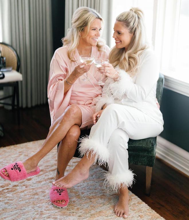 Bride clinking her drink with another woman in a pink satin robe. 