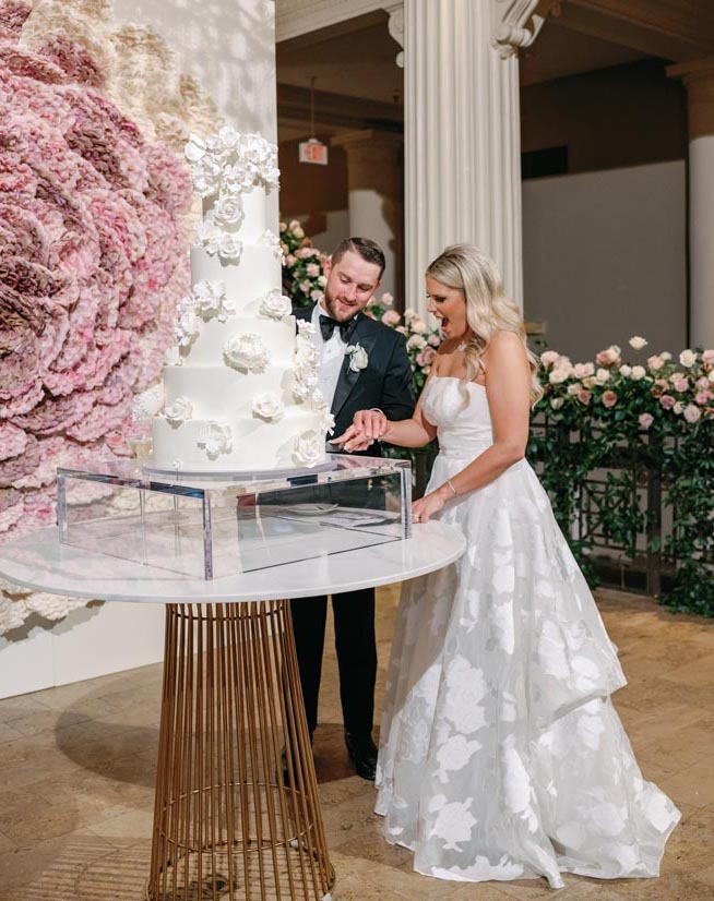 The bride and groom cutting into their five tier floral white cake. 