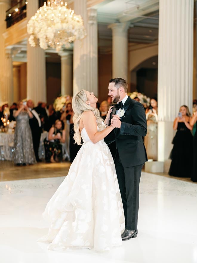 The bride and groom dancing on the dance floor with guests watching behind them.