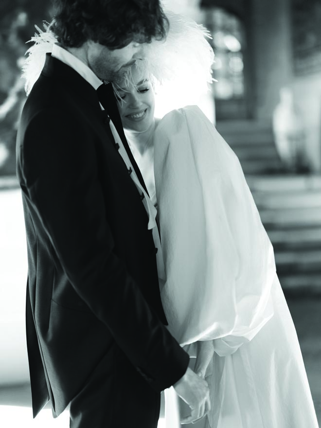 The bride hugging the groom with her white feather hat on. 