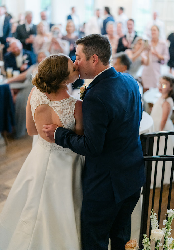 Bride and groom kissing on the stairs with guests clapping for them. 