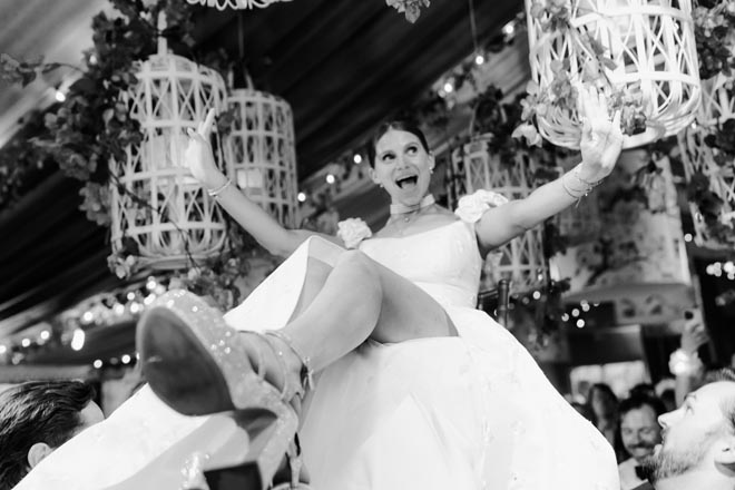 The bride being lifted in her chair by guests. 