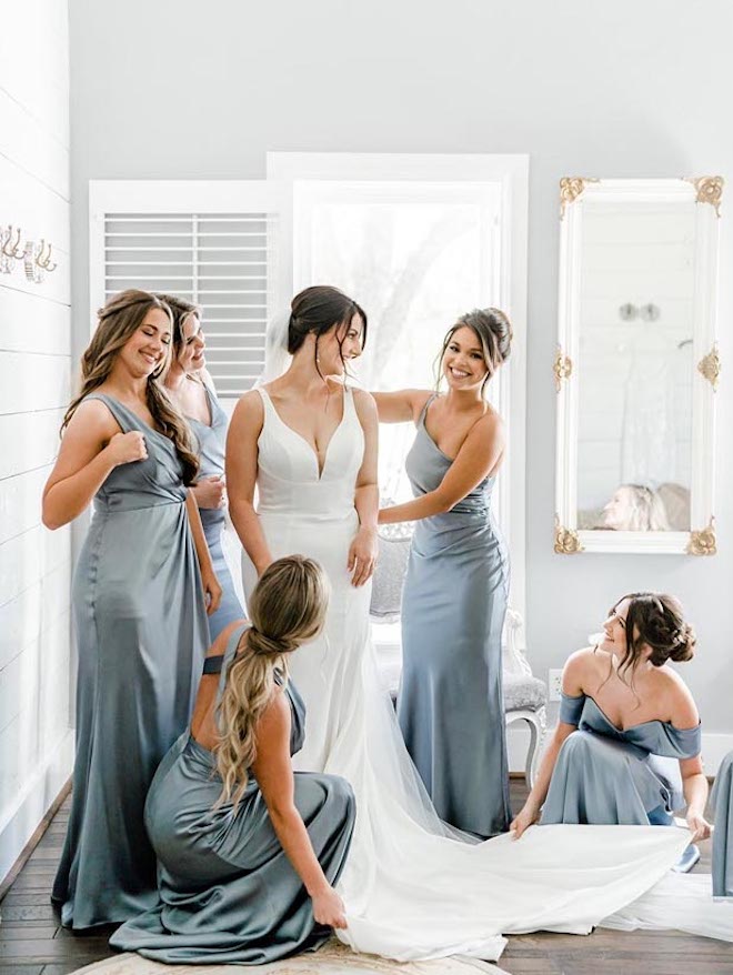 The bridesmaids help the bride put on her wedding dress. 