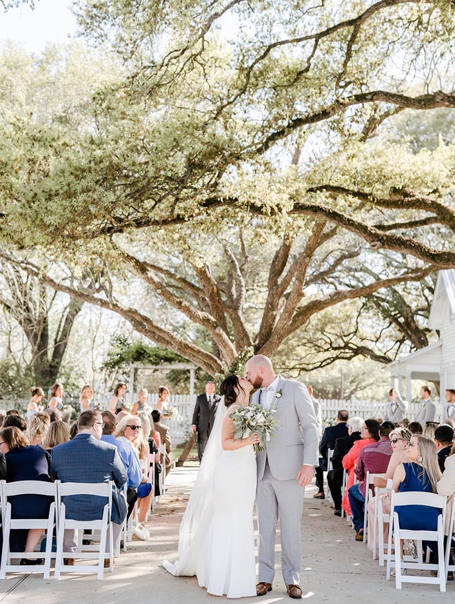 The bride and groom share a kiss at the end of the aisle after exchanging vows with a countryside wedding. 