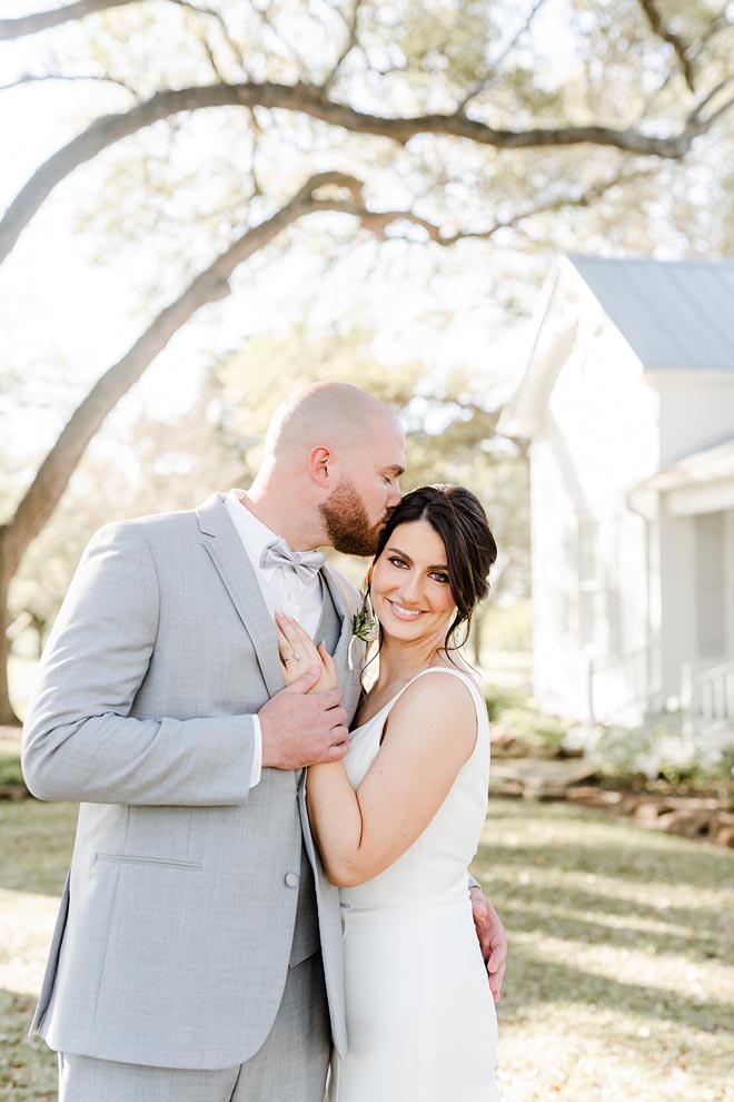 The groom gives the bride a kiss on her head at their charming French blue wedding. 