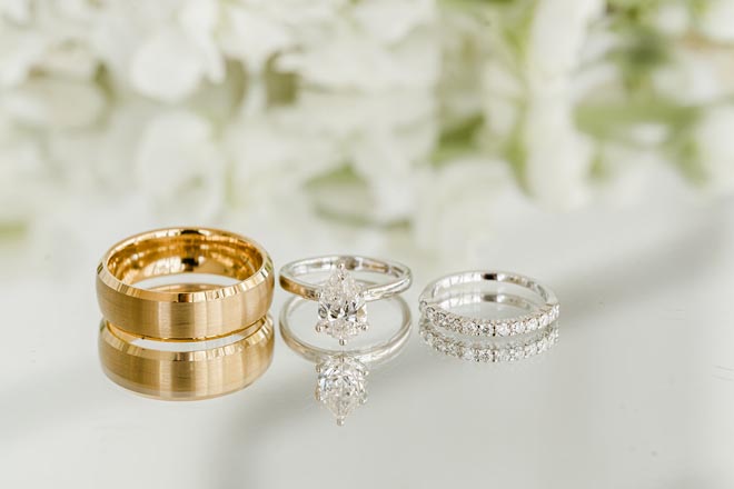 The bride and groom's wedding bands and wedding ring lay on top of a mirrored surface. 