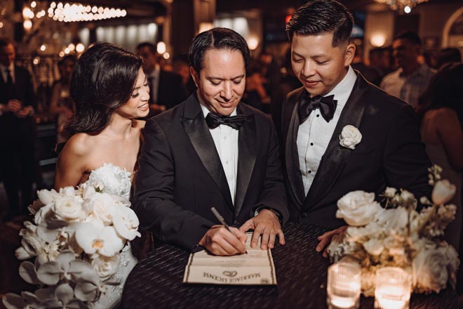 At their wedding reception, the bride and groom watch their marriage license be signed.