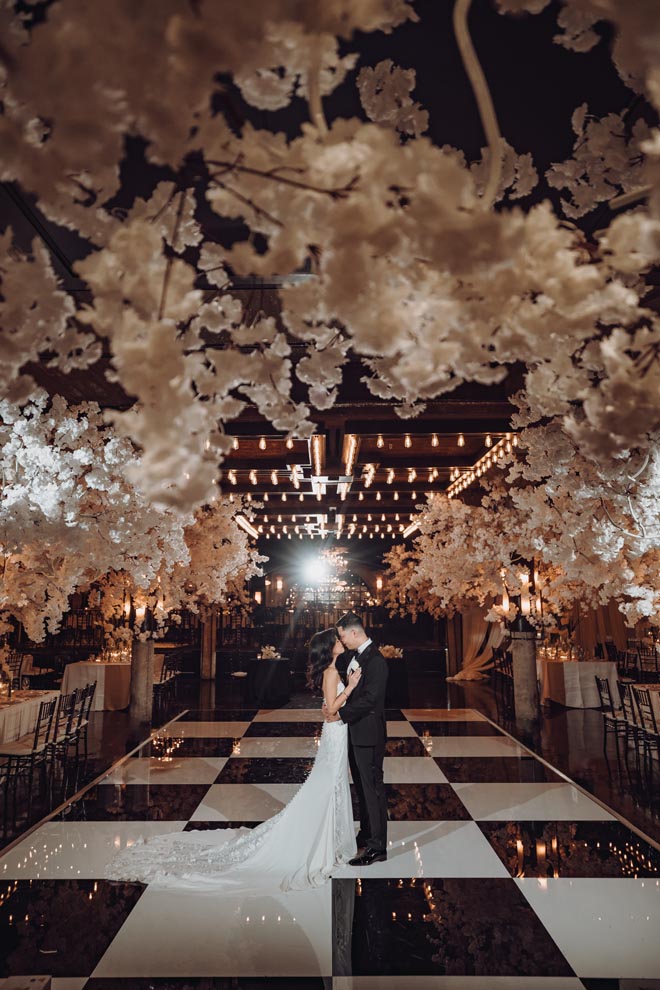 The bride and groom stand on a white and black checkered dancefloor at their wedding reception.