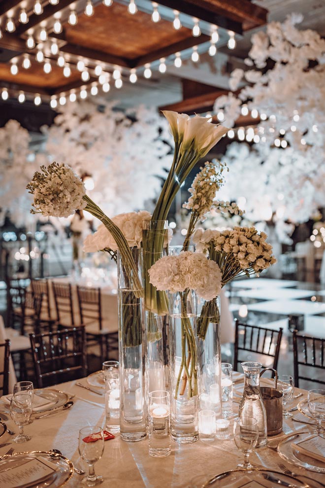 Various white florals in glass vases detail the reception tables at the wedding venue, The Astorian.