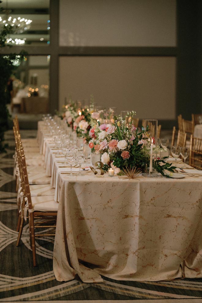 Vibrant florals and candlelight detail the wedding party's table at the wedding reception.