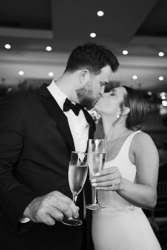 The bride and groom share a kiss while toasting with a glass of champagne. 