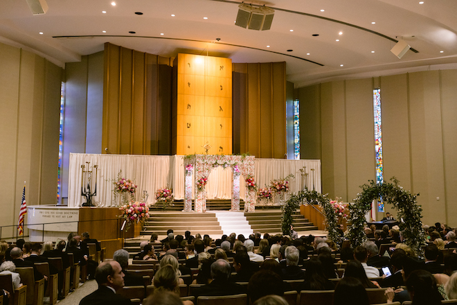 Green archways leading to a floral print Chuppah.