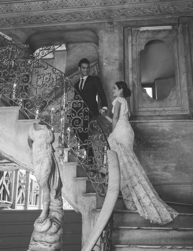 The groom leading the bride up a staircase with intricate architecture. 