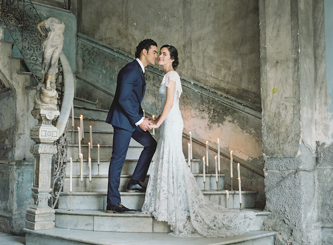 A bride and groom holding hands on stairs lined with candles in an old building. 