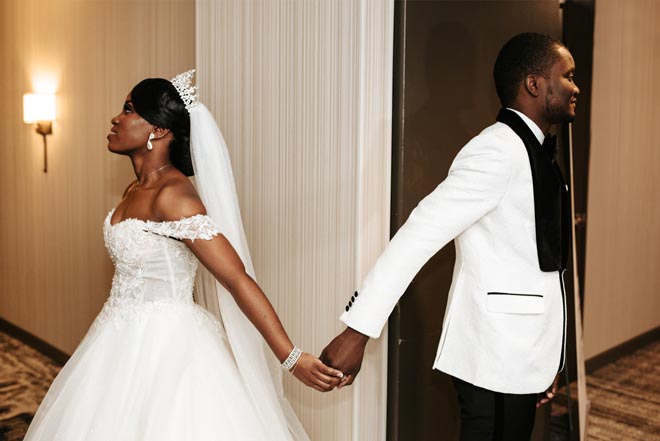 The bride and groom stand behind separate walls and hold hands before walking down the aisle. 