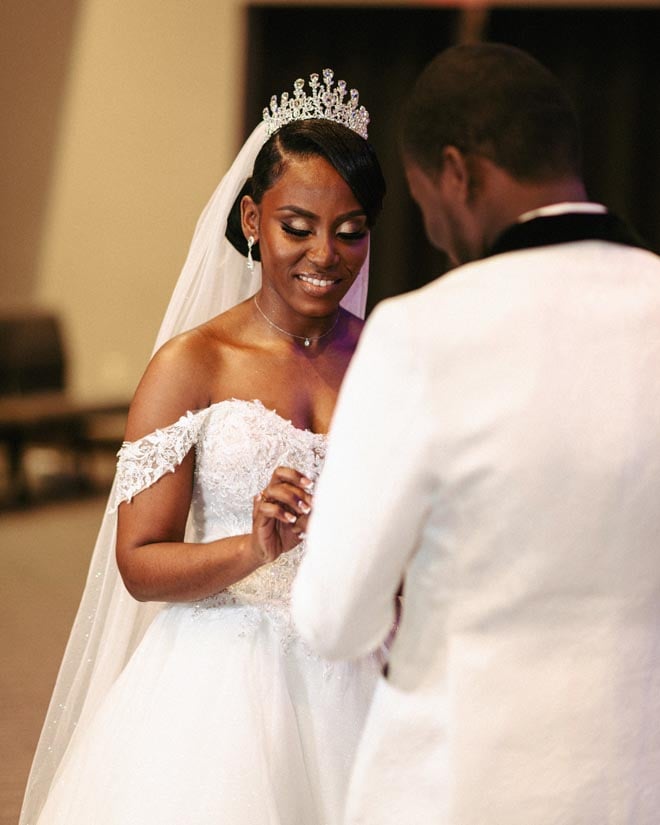 The bride puts the groom's wedding band on his finger. 