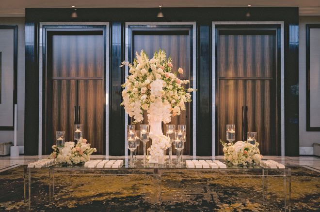 Blush, white and greenery florals detail the table at a ballroom wedding reception.