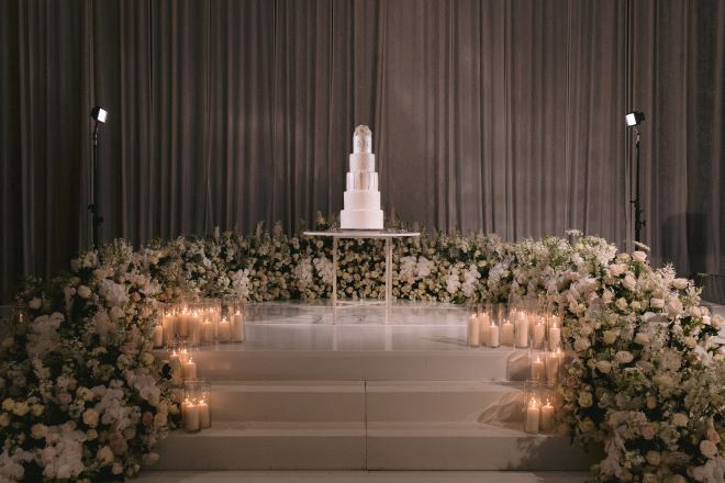 A large floral installation surrounds a five-tier white wedding cake at the wedding reception.