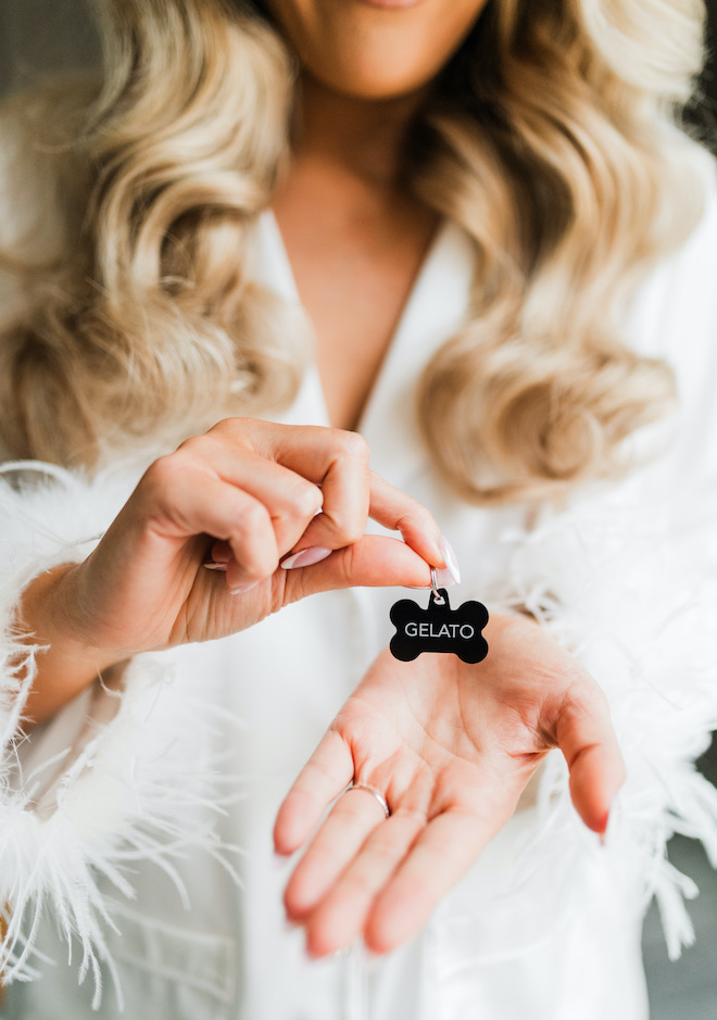 A bride wearing white satin-feathered pajamas with a dog name tag reading "Gelato" in her hands. 