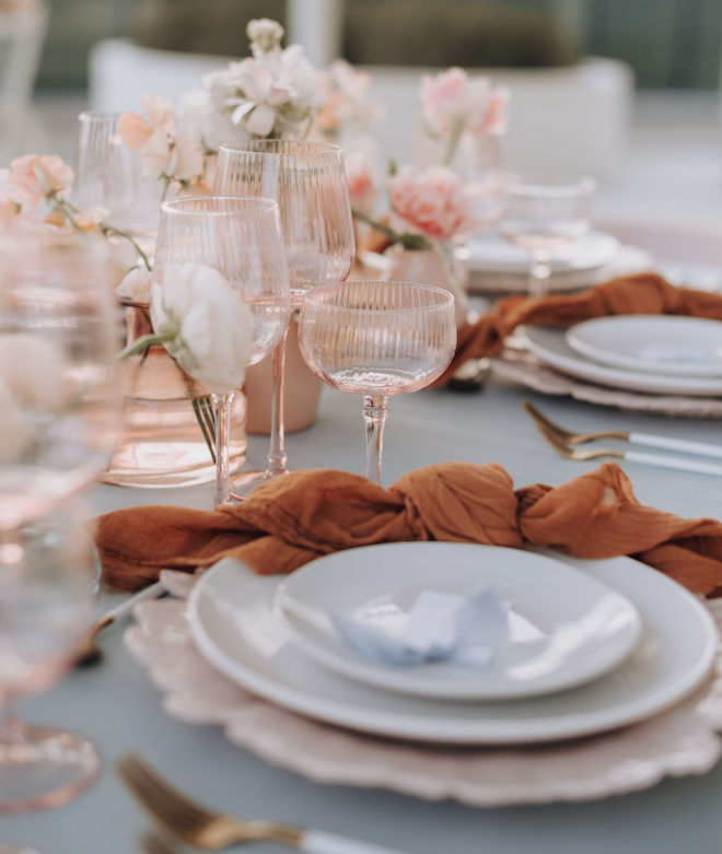 Tablescape decor with white plates, peach glassware and orange napkins. 