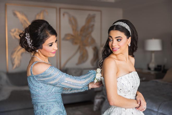 The bride's mother zips her into her wedding dress. 