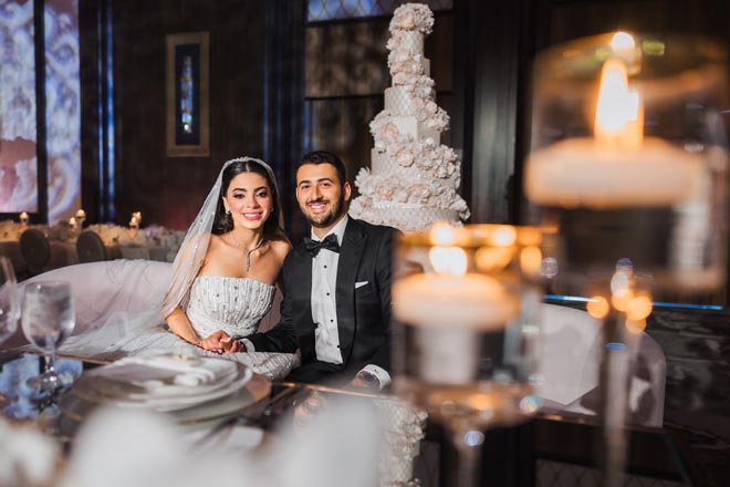 The bride and groom smile in front of their 8-tier wedding cake designed by Cakes by Gina. 