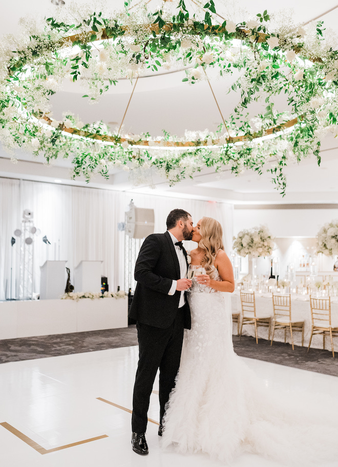 The bride and groom kissing on the white and gold dance floor. 