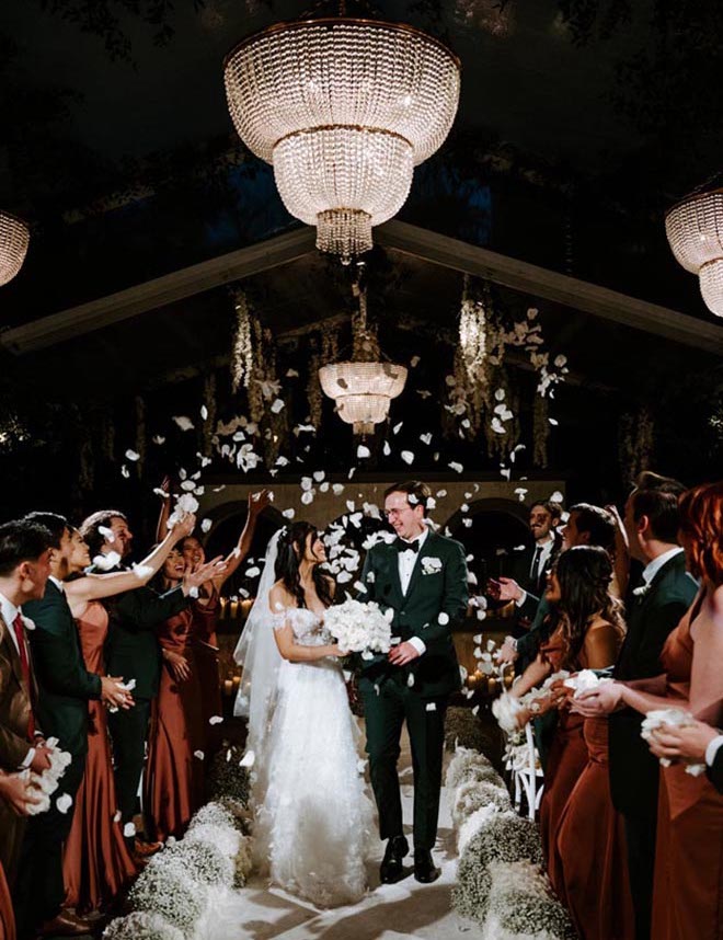 The wedding party throw white rose petals at the bride and groom as they walk down the aisle. 