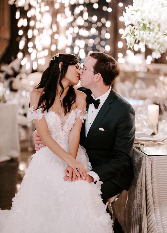 The bride sits on the groom's lap to share a kiss.