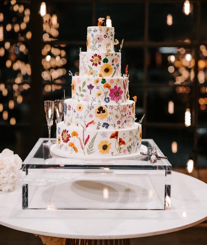 A five-tier wedding cake is hand-painted in yellow and pink flowers. 