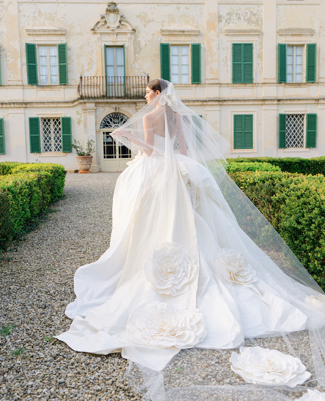 Model wearing a strapless ballgown and a cathedral length veil with large floral embellishments. 