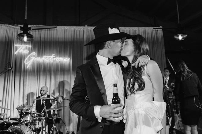 The bride and groom share a kiss under a neon sign that says their last name.