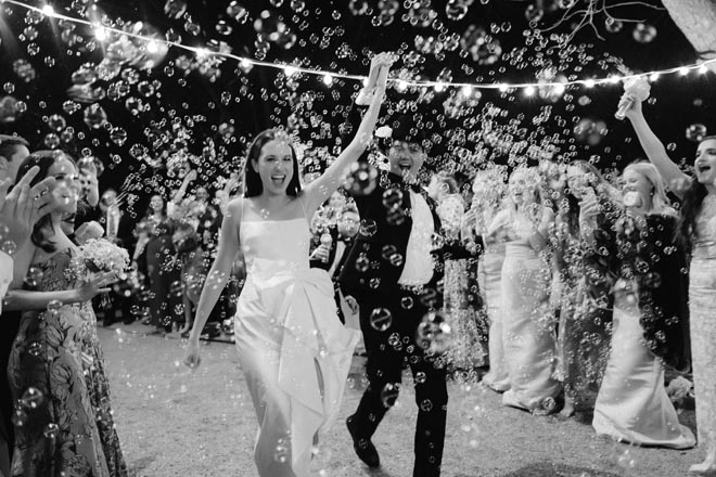 The bride and groom hold hands as they exit their wedding with a bubble send-off.