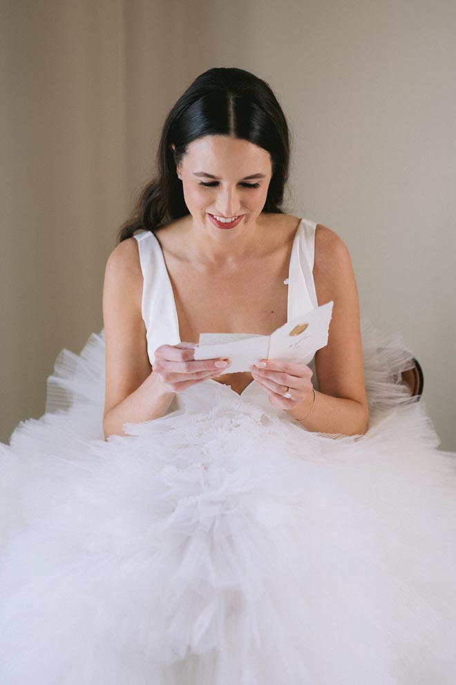 The bride sits in a chair as she reads a letter from the groom. 