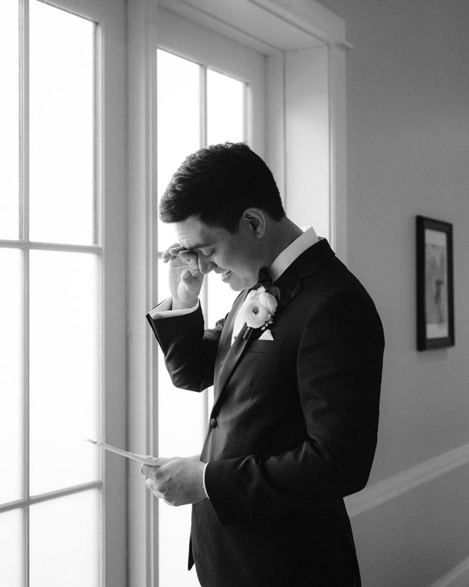 The groom wipes his tears as her reads a letter from the bride. 