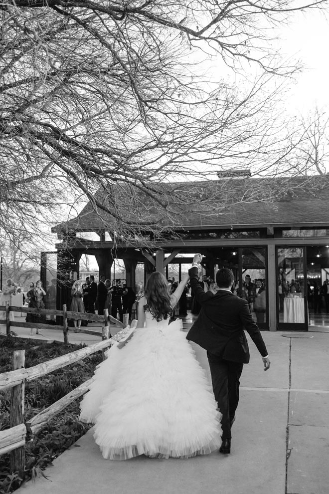 The bride and groom hold hands as they walk into their ballroom wedding reception.