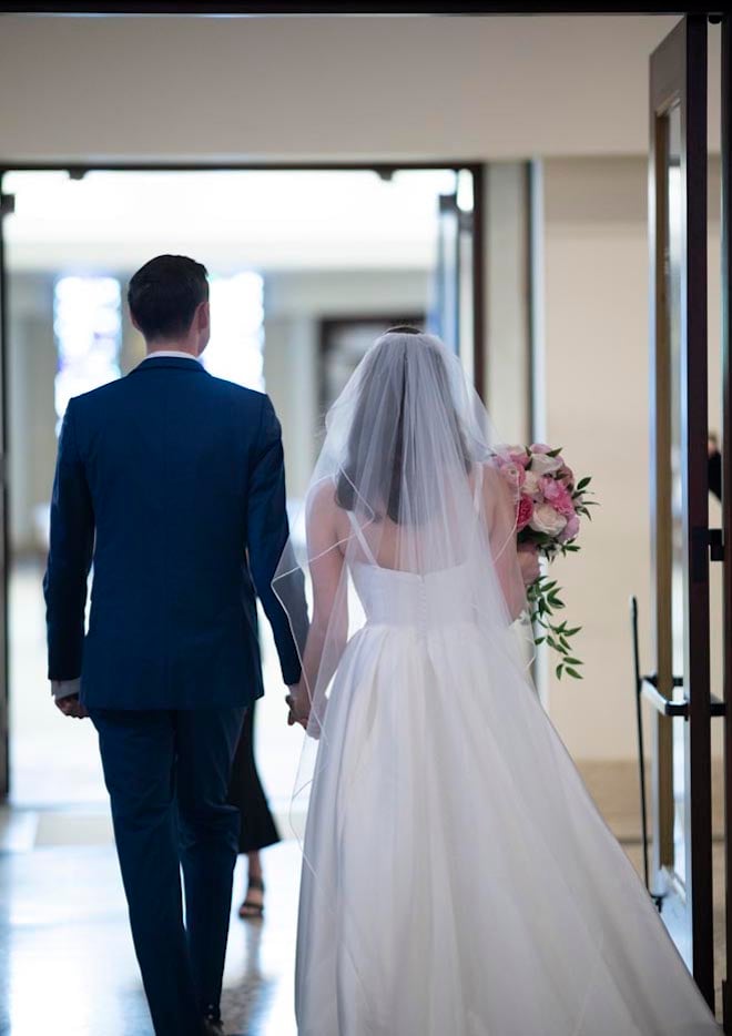 The bride and groom walk out of the church holding hands. 