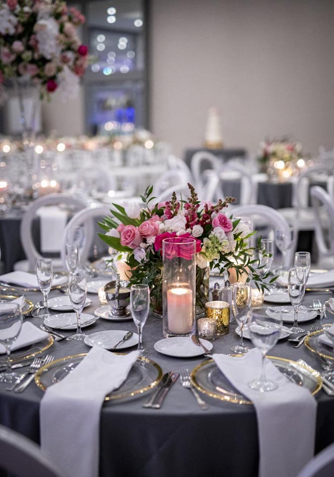 Pink floral centerpieces, gold chargers and navy linens decorate the wedding reception tables.