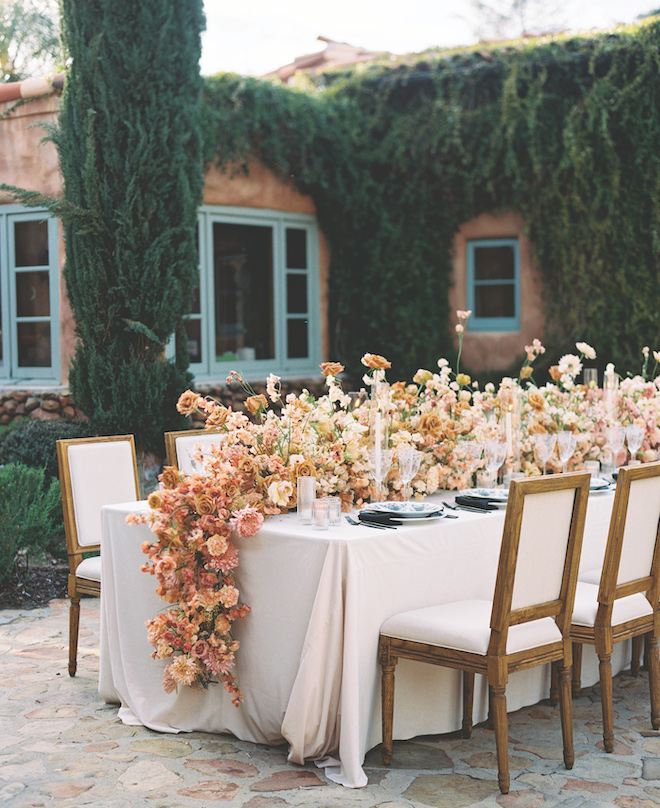 Orange and peach hued florals in the center of a reception table. 