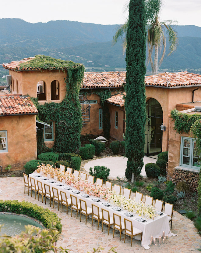 A long reception table with ombre peach and yellow florals in front of the terracotta wedding venue in Ojai. 