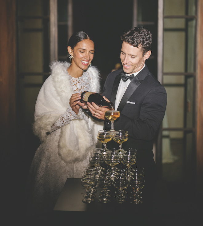 The bride and groom pouring champagne into a tower of coupe glasses. 