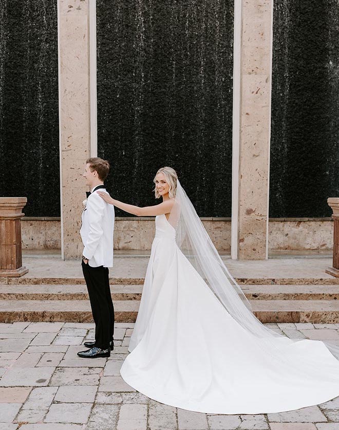 The bride placing a hand on the groom's shoulder before their first look in front of the water wall at The Bell Tower on 34th. 