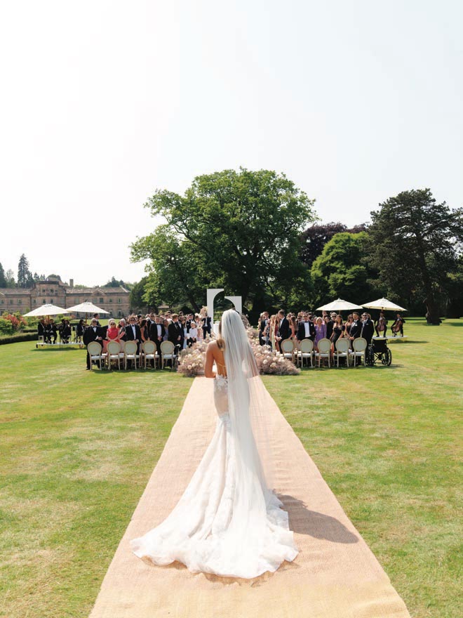 The bride walks down the aisle wearing a Berta wedding dress for her outdoor wedding ceremony.